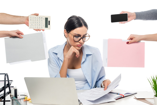 Przemyślana bizneswoman pracująca w pobliżu współpracowników z dokumentami, kalkulatorem i smartfonem na białym - Zdjęcie, obraz