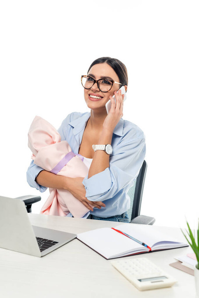 szczęśliwy bizneswoman gospodarstwa niemowlę dziecko podczas rozmowy na smartfonie w miejscu pracy odizolowany na biały - Zdjęcie, obraz
