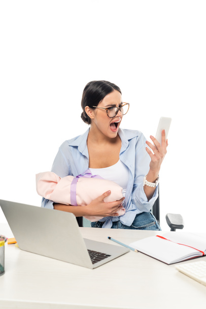 irritated businesswoman screaming while holding smartphone and baby at workplace isolated on white - Fotografie, Obrázek