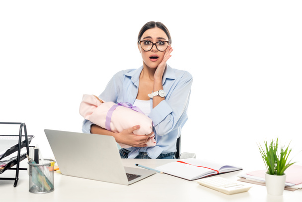 shocked businesswoman touching face while sitting at workplace with newborn baby isolated on white - Photo, Image