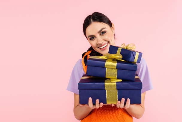 joyful woman holding presents while smiling at camera isolated on pink - Фото, зображення