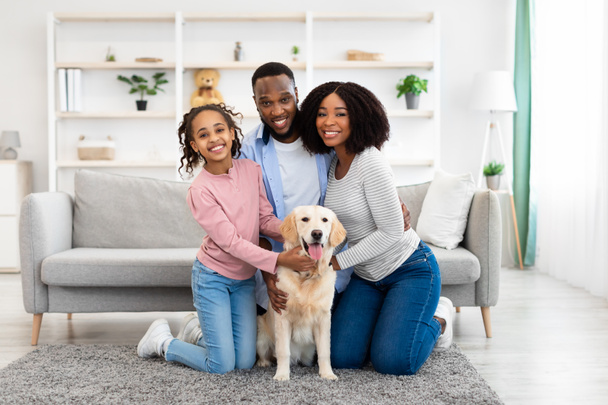 Молодая чёрная семья обнимает собаку, позирующую дома - Фото, изображение