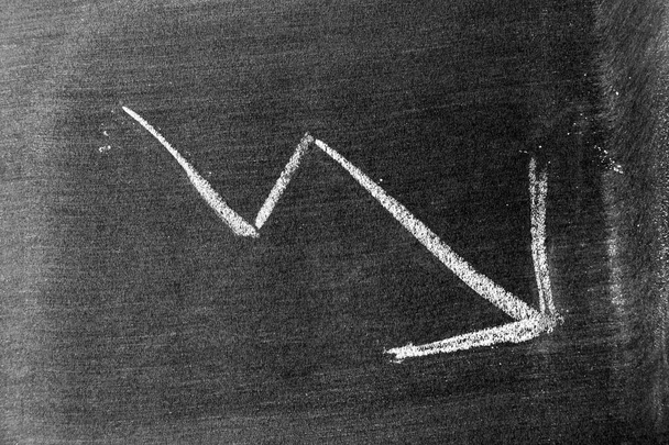 Dibujo de mano de tiza blanca en forma de flecha hacia abajo en pizarra o pizarra de fondo (Concepto de declive de acciones, tendencia a la baja de los negocios, economía) - Foto, Imagen