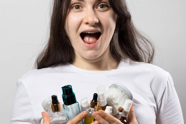 A happy girl holds a lot of makeup in her hands. An abundance of decorative and care cosmetics, jars and tubes for advertising shop, offer or sale. - Photo, Image