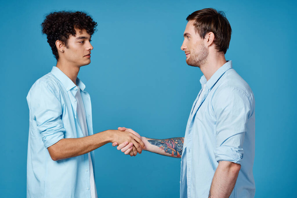 кудрявый парень в рубашке стоит рядом с молодым человеком в футболке на голубом фоне обрезанный вид - Фото, изображение