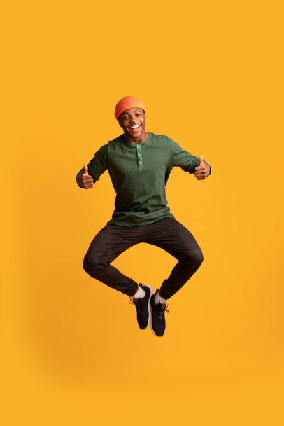 gelukkig opgewonden zwart guy springen en tonen duimen omhoog bij camera - Foto, afbeelding
