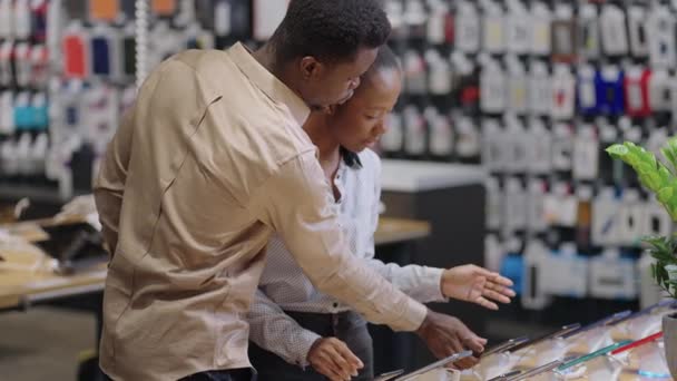giovani afro-americani stanno facendo shopping in negozio di attrezzature digitali, uomo e donna stanno scegliendo smartphone - Filmati, video