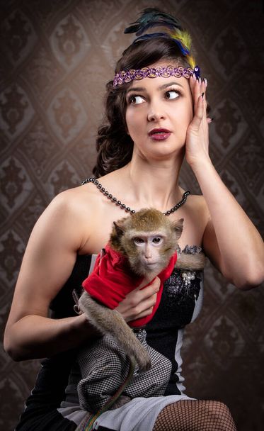 Retrato femenino retro en el estilo de los años 20 o 30. Una hermosa dama sostiene a un pequeño mono. - Foto, imagen