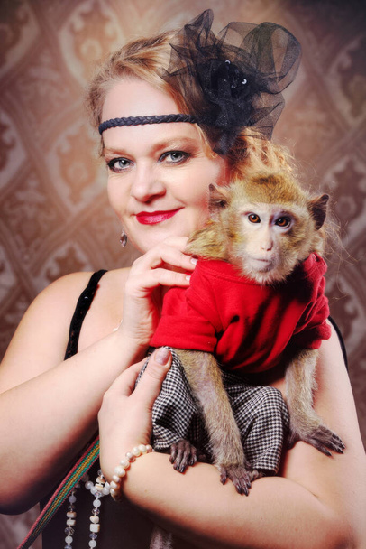 Retro female portrait in the style of 20s or 30s. A gorgeous lady is holding a little monkey. - Fotoğraf, Görsel