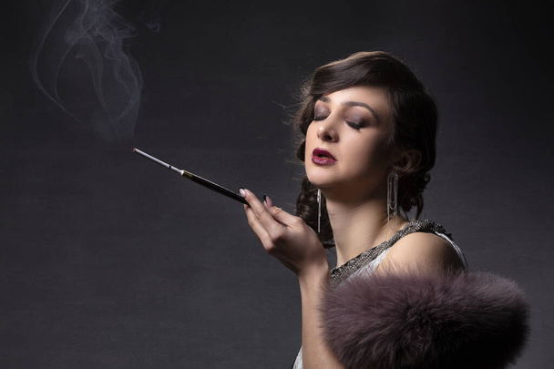 Retro woman portrait. A beautiful woman in the style of the 20s and 30s with a cigarette holder smokes. - Φωτογραφία, εικόνα
