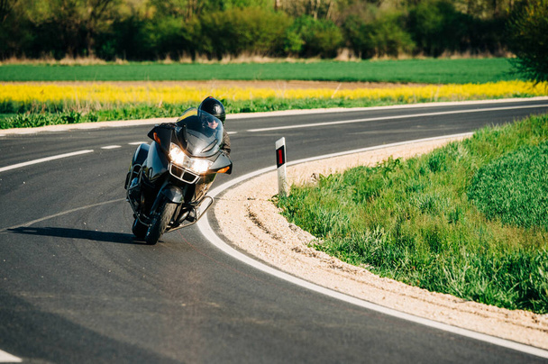 Водитель мотоцикла едет один по асфальтовой дороге. Стилистическое фото байкера в движении на пустой дороге - Фото, изображение