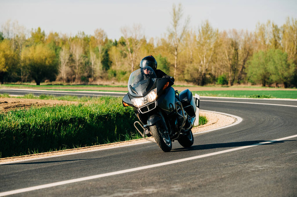 Motorcycle driver riding alone on the asphalt road. Lifestyle photo of a biker in the motion at the empty road - Photo, Image