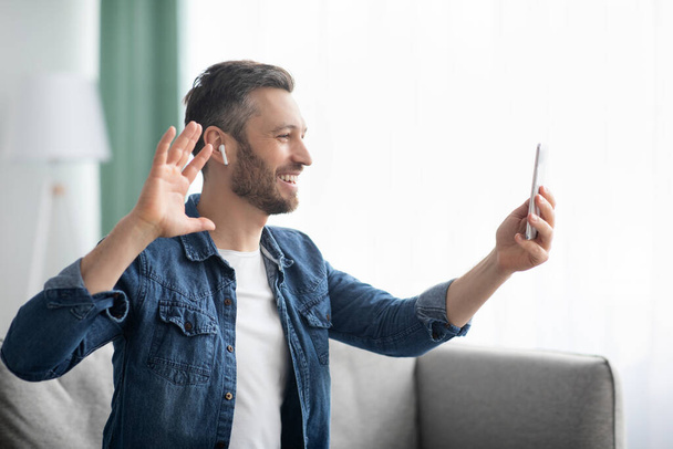 Cheerful bearded man waving at mobile phone, having video call - Foto, afbeelding