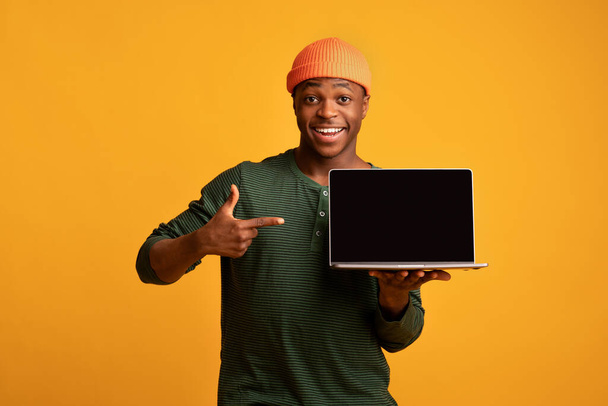 Ωραία ιστοσελίδα. Χαρούμενος Αφρικανός που δείχνει τον φορητό υπολογιστή με μαύρη οθόνη - Φωτογραφία, εικόνα