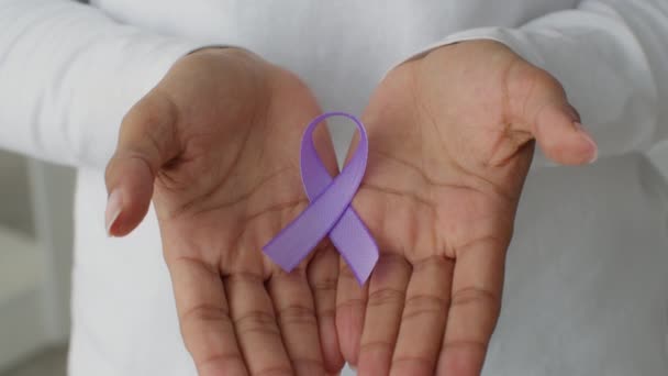 Symbol świadomości przemocy domowej. Zbliżenie ujęcia fioletowej wstążki w nierozpoznawalnych rękach kobiety - Materiał filmowy, wideo