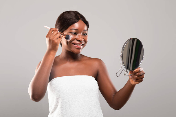 Щаслива молода чорна жінка тримає макіяж пензлем і дивиться в дзеркало
 - Фото, зображення