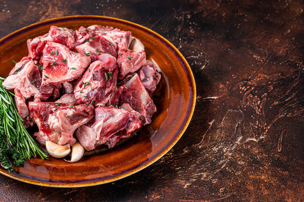 Сырое баранино, нарезанное на гуляш или тушеное мясо с костью на деревенской тарелке. Темный фон. Вид сверху. Копирование пространства - Фото, изображение