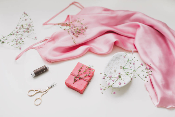 Composition with pink silk fabric, gift in craft paper and threads and scissors on white background. Flat lay, top view. Hobby, leisure concept. - Foto, Imagem