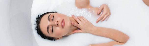 чувственная женщина трогает шею, принимая ванну с молоком, баннер - Фото, изображение