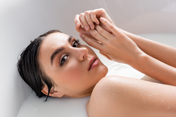 csinos nő kéz a kézben az arc mellett, miközben pihentető fürdés tejjel - Fotó, kép
