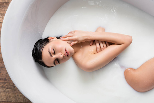 top view of sensual woman touching neck while enjoying milk bath - Foto, Imagem