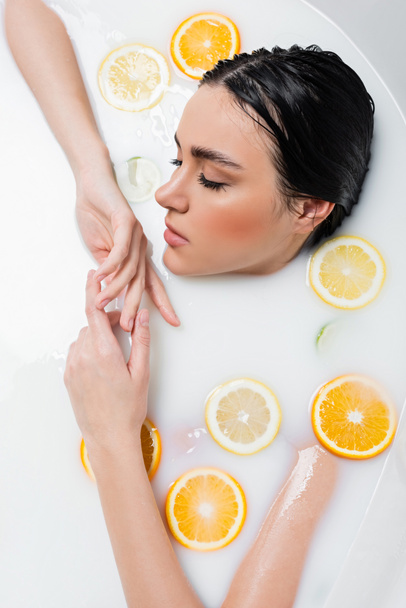 top view of woman taking milk bath with lemon and orange slices - Foto, afbeelding