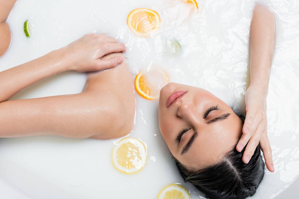 ミルクとスライスされた柑橘系の果実を持つお風呂の若い女性のトップビュー - 写真・画像