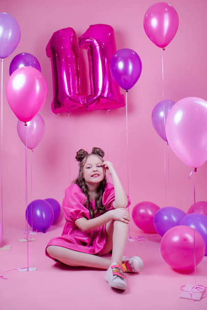 gyönyörű lány rózsaszín smink és rózsaszín bőr ruha. közel színes léggömbök alakja tizenegyedik 11 rózsaszín háttér. koncepció születésnapi party ünneplés - Fotó, kép