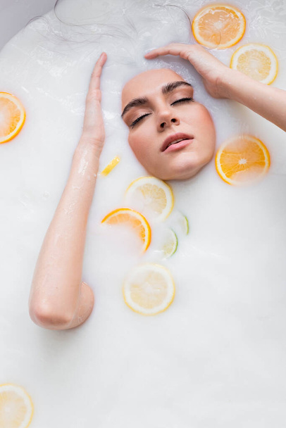 csinos nő csukott szemmel fürdés tejben szeletelt citrusszal - Fotó, kép