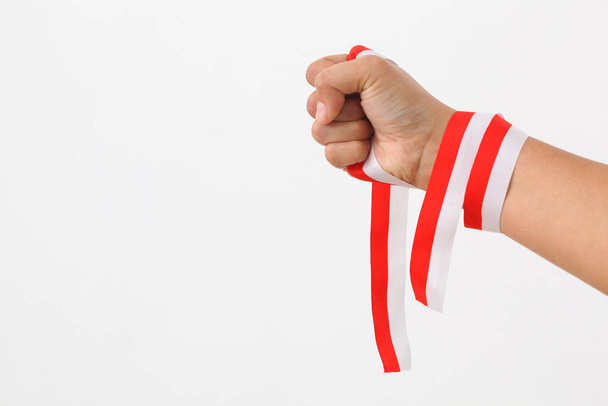 A human hand holds red white ribbon as symbol of the Indonesian flag. Isolated on white background - Foto, immagini