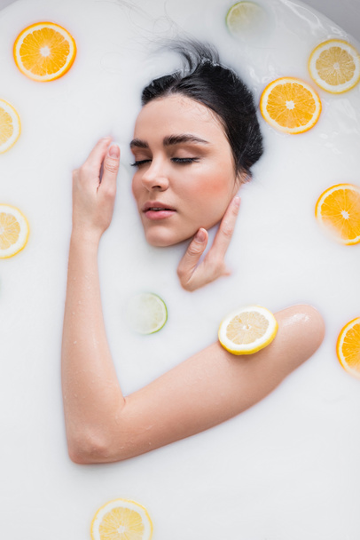 young sensual woman taking milk bath with sliced citrus fruits - Foto, afbeelding