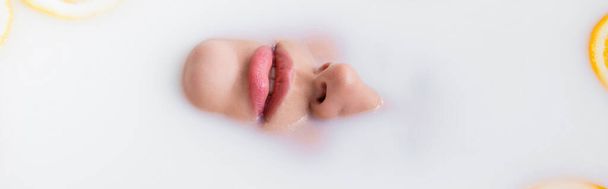 bovenaanzicht van vrouwelijk gezicht ondergedompeld in melkbad, banner - Foto, afbeelding