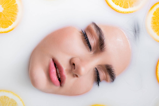 close up view of female face with closed eyes in milk bath with citrus fruits - Foto, Imagen