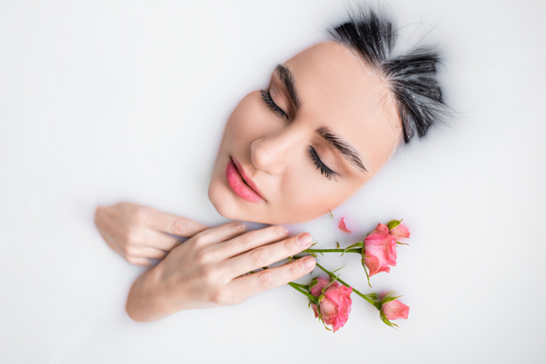 junge Frau mit geschlossenen Augen und rosa Rosen, die in Milch badet - Foto, Bild