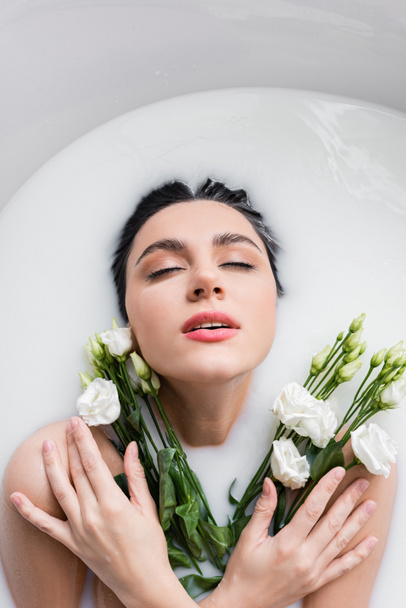 femme séduisante avec des fleurs d'eustomie appréciant se baigner dans le lait - Photo, image