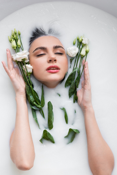 pretty woman with closed eyes enjoying bathing in milk with eustoma flowers - 写真・画像