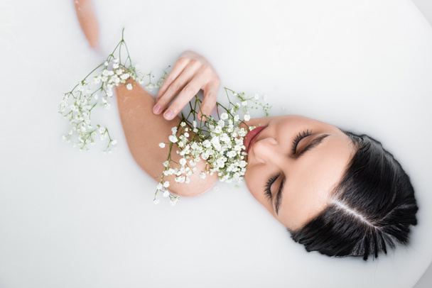 vista superior de jovem, mulher sensual desfrutando de banho de leite com flores de gypsophila - Foto, Imagem