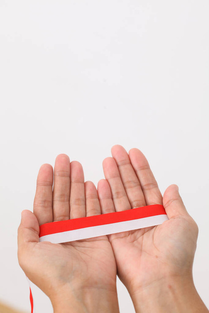 Ludzka ręka trzyma czerwoną białą wstążkę jako symbol indonezyjskiej flagi. Izolacja na białym tle - Zdjęcie, obraz