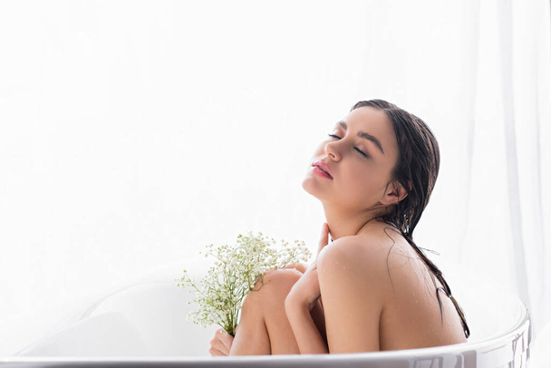 bonita mujer bañándose con los ojos cerrados y flores blancas, minúsculas - Foto, imagen
