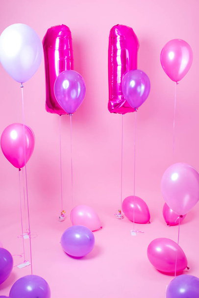 πολύχρωμα μπλε, ροζ και μοβ μπαλόνια κοντά σε αερόστατα σχήμα νούμερο έντεκα. σε ροζ φόντο. έννοια του εορτασμού πάρτι γενεθλίων. - Φωτογραφία, εικόνα