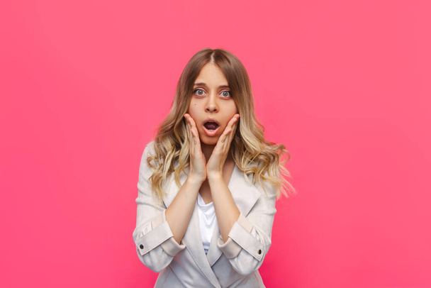 A young beautiful caucasian impressed surprised shocked blonde woman with wavy hair in a stylish clothing surprised by the news about a sale and discounts isolated on a bright color pink background - Φωτογραφία, εικόνα