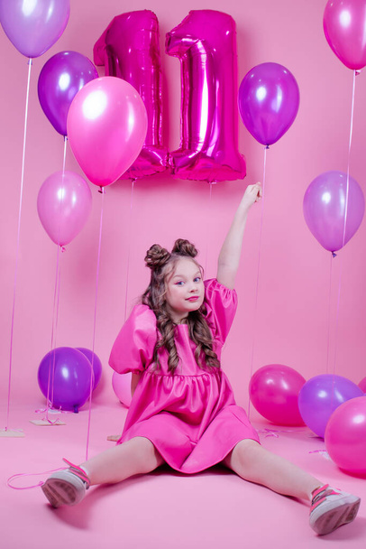 sweet brunette girl with pink make up and in pink leather dress. near colorful balloons in shape of number eleven. on pink background.concept of joy, party, birthday celebration - Photo, Image