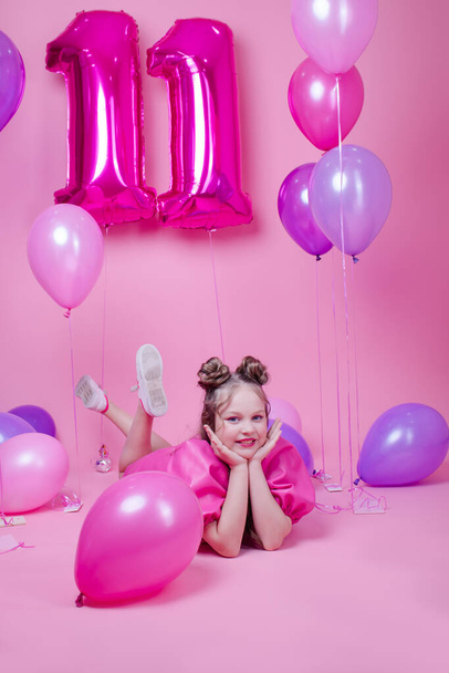 sweet brunette girl with pink make up and in pink leather dress. near colorful balloons in shape of number eleven. on pink background.concept of joy, party, birthday celebration - Fotó, kép