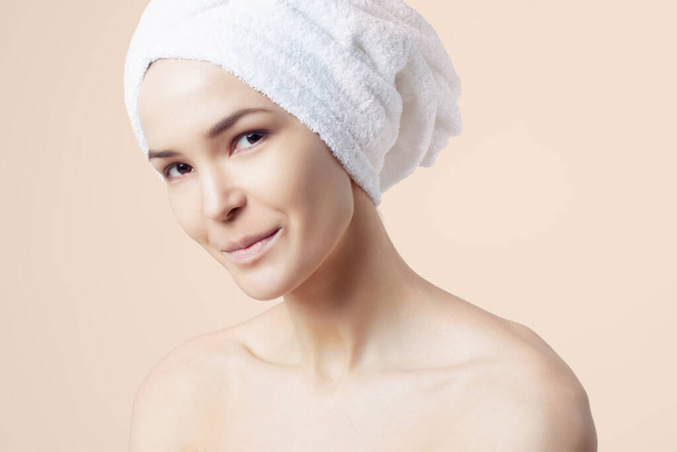 Cute positive girl in towel on her hair on beige background. Cleansing, moisturizing, course for the skin of the face - Valokuva, kuva