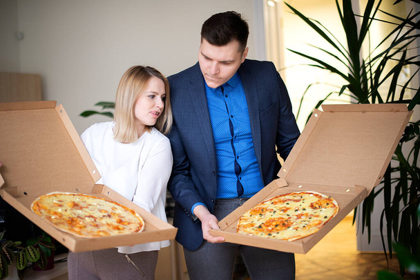 Młoda atrakcyjna para-kobieta i mężczyzna trzymający dwa duże otwarte pudełka pizzy, szybki lunch lub obiad w biurze lub w domu - Zdjęcie, obraz