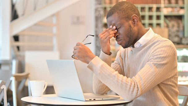 Uomo africano stressato con il computer portatile che ha mal di testa in Cafe - Foto, immagini