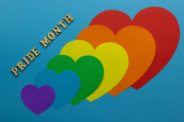 Rainbow heards symbolize gay and LGBT pride on a blue background. PRIDE month. A phrase made of wooden letters. - Photo, Image
