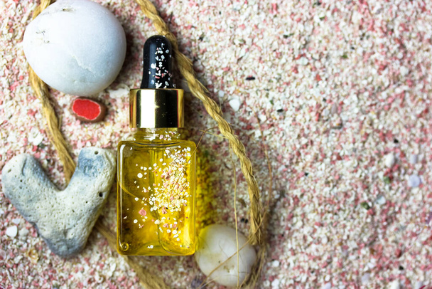 Yellow oil serum essence in glass bottle flatly. Sunscreen oil to protect the face, body at summer days. Sea theme, seashells, stones, pink sand. Concept of natural cosmetic, trendy beauty skin care.  - Photo, image