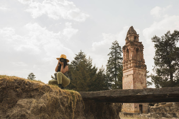 Avontuurlijk meisje met gele hoed die foto 's maakt in de ruïnes van een oude kerk midden in het bos - Foto, afbeelding