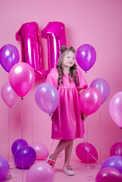 sladká brunetka dívka s růžovou make-up a v růžových kožených šatech. téměř barevné balónky ve tvaru jedenáctky. na růžovém pozadí.koncept radosti, párty, narozeninová oslava - Fotografie, Obrázek